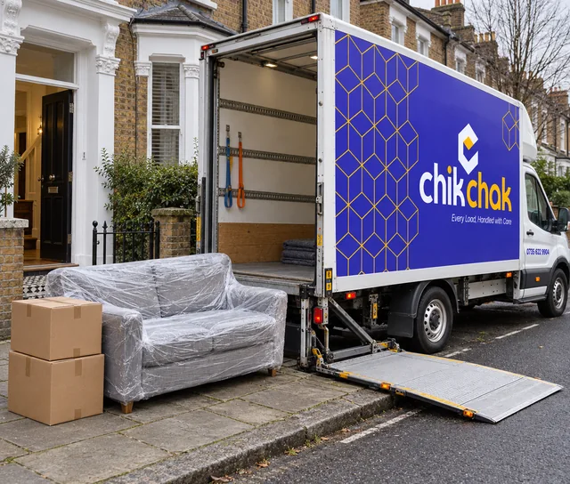 The chikchak van at the kerb with its tail lift down, a wrapped sofa and boxes by an open front door